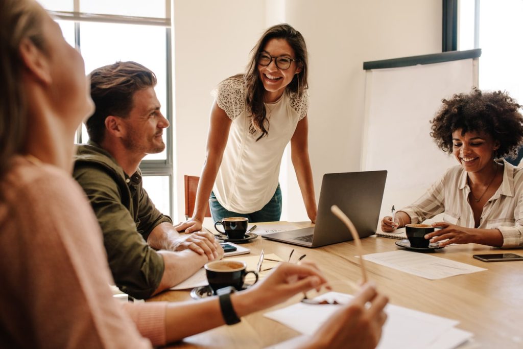 Casual business meeting with woman standing up smiling at colleagues